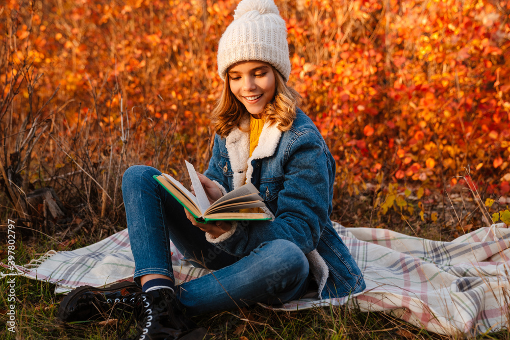 Happy girl sitting outdoors in autumn park and reading book Happy girl sitting outdoors in autumn park and reading book