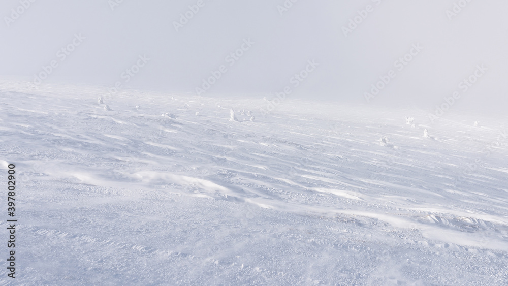 The mountain slope is completely covered with a layer of snow with traces of the wind on it.