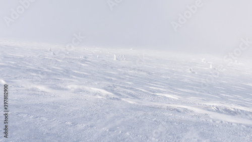 The mountain slope is completely covered with a layer of snow with traces of the wind on it.