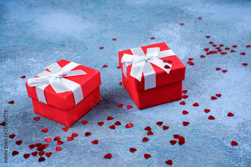 Two red gifts, heart shape confetti on blue concrete background. Valentine, love, card, invitation concept. Close-up, copy space