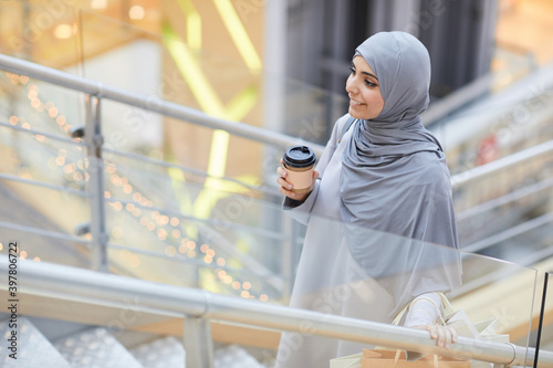 Photography Portrait of smiling Middle-Eastern woman holding coffee cup while going up stair