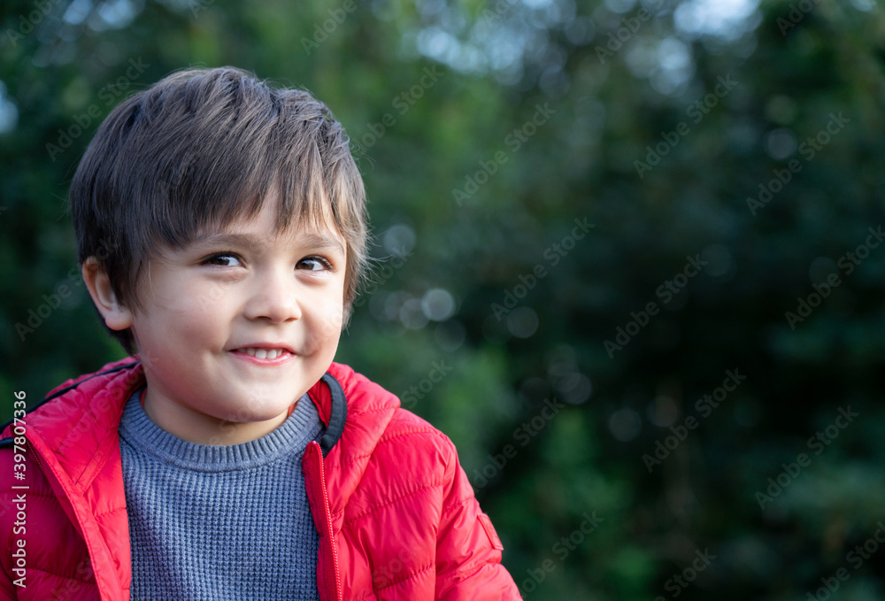 Happy kid looking at camera and smiling face with blurry green bokeh background,Cute boy with red jacket relaxing outside the park, Child playing outdoor on springtime with blurry natural background Happy kid looking at camera and smiling face with blurry green bokeh background,Cute boy with red jacket relaxing outside the park, Child playing outdoor on springtime with blurry natural background