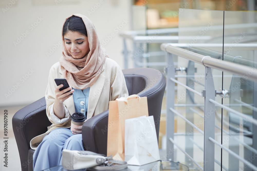 Portrait of beautiful Middle-Eastern woman wearing headscarf while using smartphone in shopping mall, copy space Portrait of beautiful Middle-Eastern woman wearing headscarf while using smartphone in shopping mall, copy space
