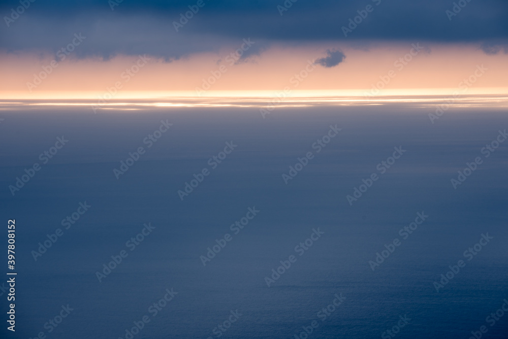surface de mer bleu gris avec une ligne horizontale de lumière à l'horizon sous des nuages gris bleus 