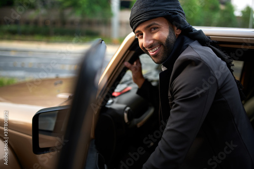 Arab man getting into luxury vehicle wearing traditional suite with keffiyeh