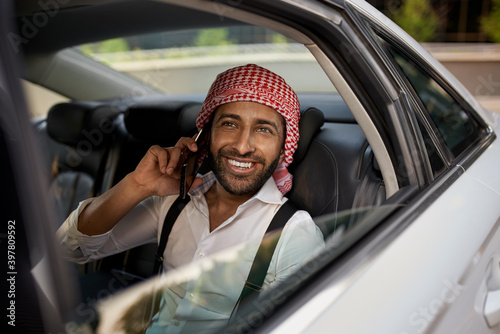 Headshot of arab businessman looking out taxi car window smiling using smartphone