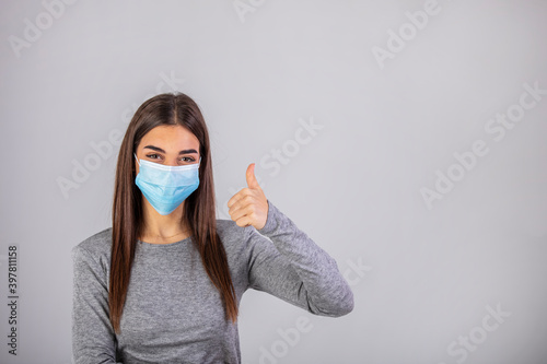 Beautiful caucasian young woman with disposable face mask. Protection versus viruses and infection. Studio portrait, concept with white background. Woman showing thumb up.