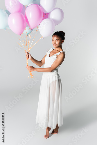 barefoot graceful african american ballerina in dress with balloons on white background