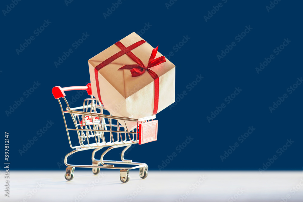 Shopping cart and gift box. Brown gift box with red bow in shopping cart on blue background, copy space
