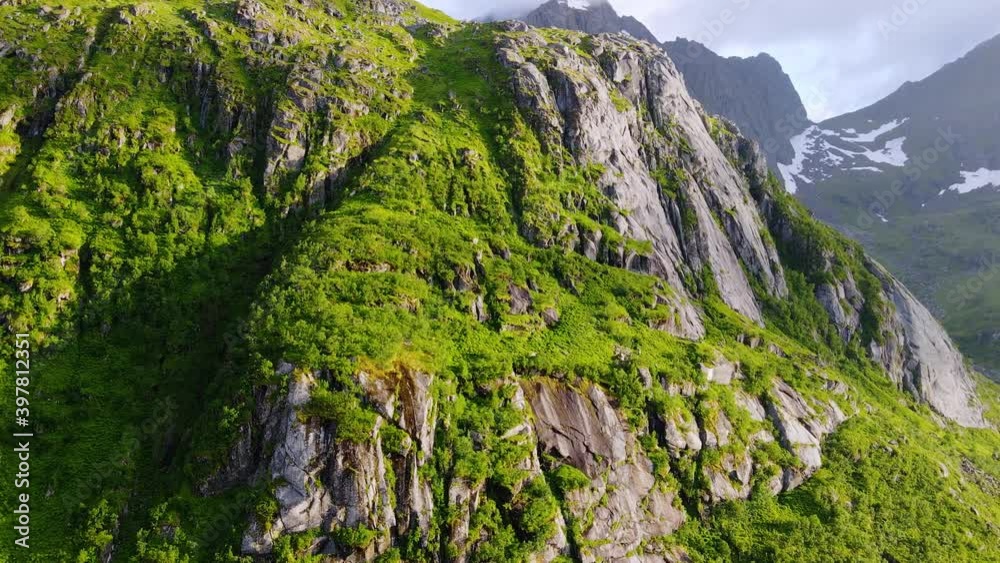 Aerial view close to a mossy, green, mountain wall, revealing the rocky coastline of Lofoten islands, Norway - pan, drone shot Aerial view close to a mossy, green, mountain wall, revealing the rocky coastline of Lofoten islands, Norway - pan, drone shot