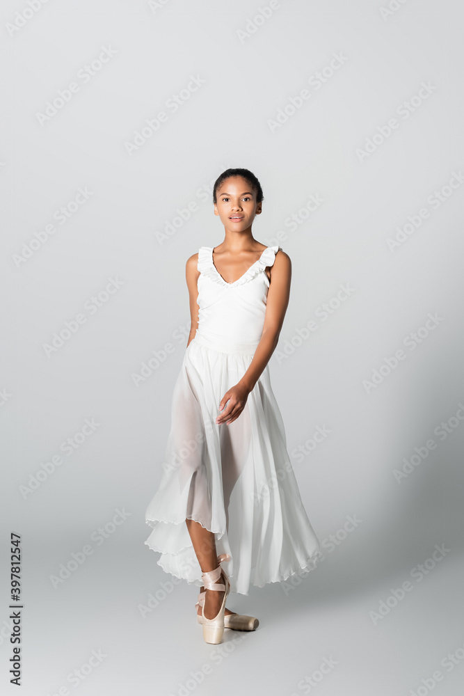 graceful african american ballerina in dress dancing on white background