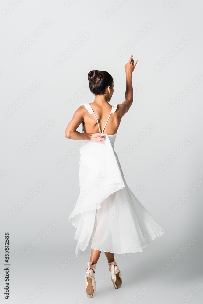 Back view of graceful African American ballerina in dress dancing on white background Back view of graceful African American ballerina in dress dancing on white background
