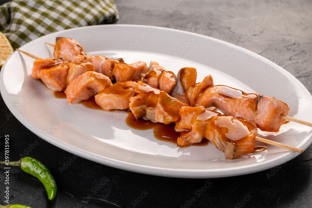 grilled salmon skewer in sauce on a white plate and dark background