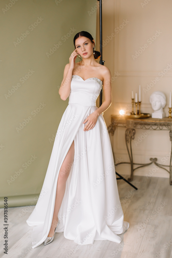 Young brunette woman stands in a white wedding dress on a green background Young brunette woman stands in a white wedding dress on a green background