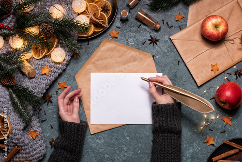 Woman writng a Christmas letter with gold pen. Workspace with brown craft envelope and ingredients for mulled wine. Winter composition, mockup photo