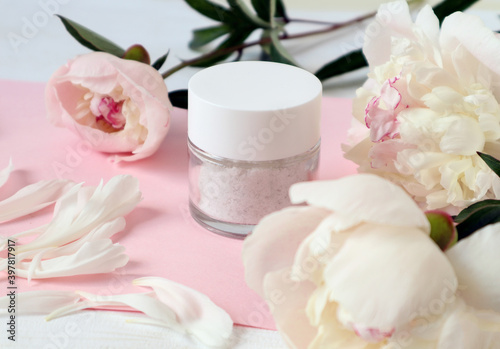 Body care cream among pastel peonies, close-up, side view - the concept of pleasant self-care