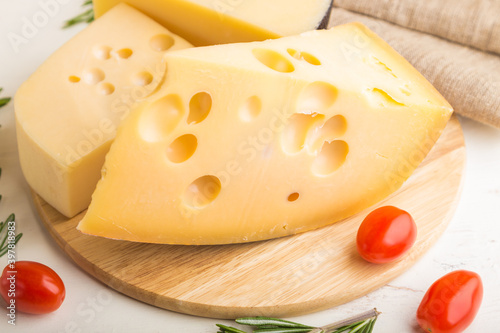 Various types of cheese with rosemary and tomatoes on wooden board on a white wooden background. Side view, close up.