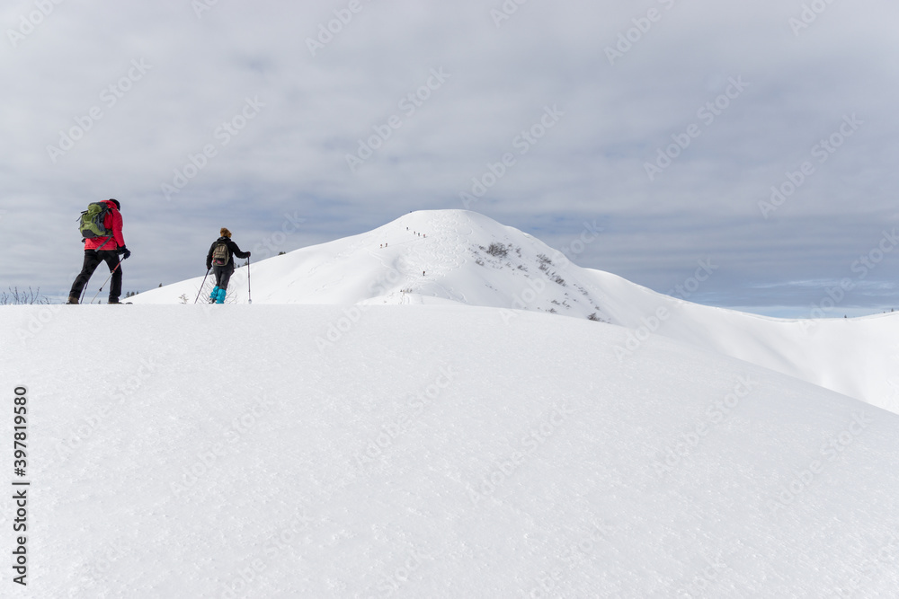 Senior couple is snowshoe hiking in alpine snow winter mountains. Allgau, Bavaria, Germany.