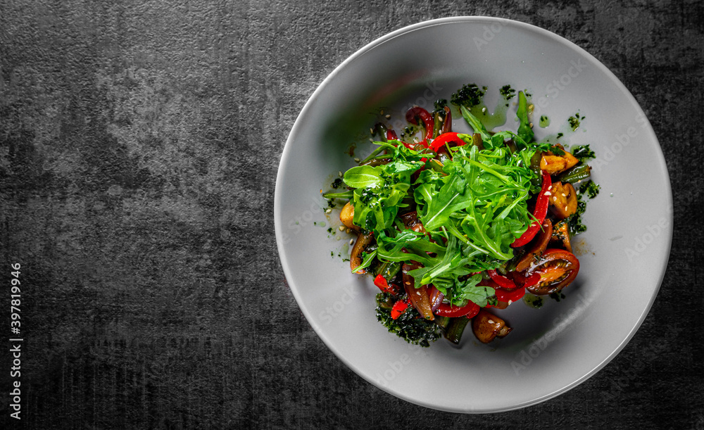 Vegetarian vegetable salad with mushrooms, arugula, tomato, beans and pepper in a bowl on Dark grey black slate background
