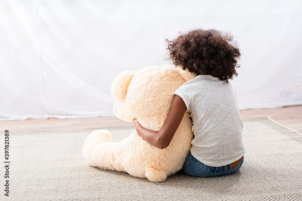 Back view of lonely african american girl with autism hugging teddy ...