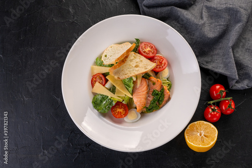 salad with salmon slices in a white plate on a dark background. Caesar salad with seafood