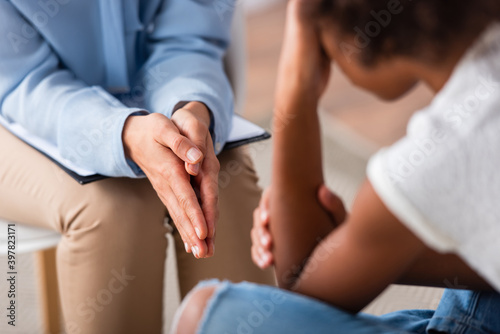 Cropped view of psychologist with praying hands sitting during consultation with blurred african american girl on foreground © LIGHTFIELD STUDIOS