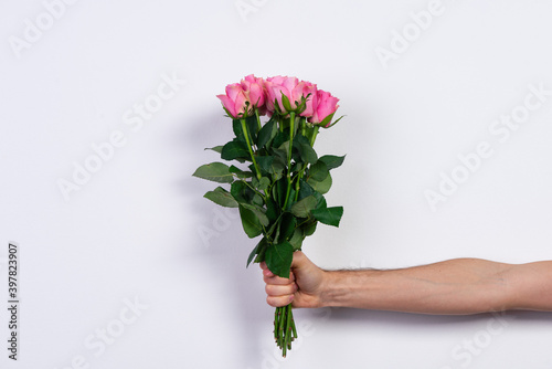Male hand holding a bouquet of pink roses on white background. © at_shoots