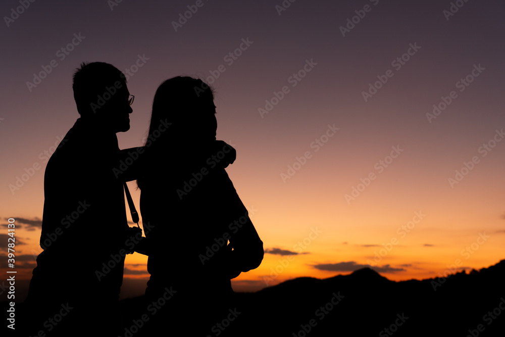 silouette of man and woman as a couple looking at sunset behind the moutain