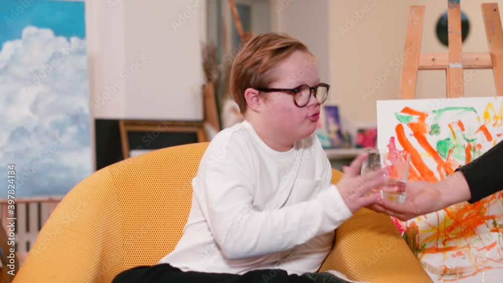 The boy drinks water from a glass. Children with Down Syndrome can have