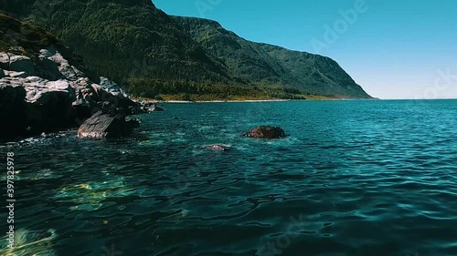 Very slow and low flight over the rocky beach. 60 FTP. Clear, azure water and sunny weather. The sea and mountains in the background. Norway 2020. photo