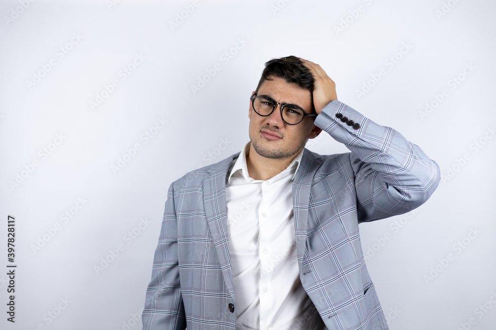 Business young man wearing suit over white background confuse and wonder about question. Uncertain with doubt, thinking with hand on head Business young man wearing suit over white background confuse and wonder about question. Uncertain with doubt, thinking with hand on head