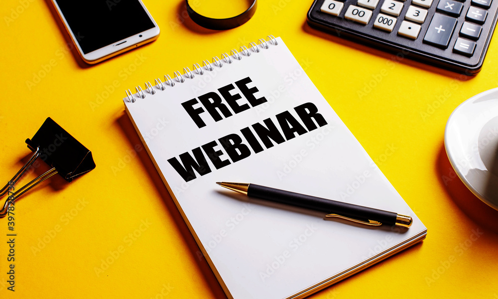 On a yellow background, a notebook with the text FREE WEBINAR, coffee, calculator, telephone and a clip for papers. Business concept