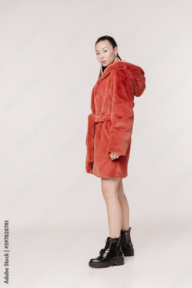 Beautiful and stylish girl with makeup in a fur coat emotionally with a smile posing on a white background