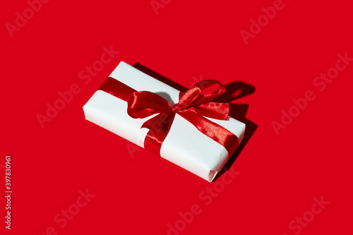 Valentine day gift. Long-distance care package. Holiday surprise. Present wrapped in white box with ribbon bow isolated on red copy space background.
