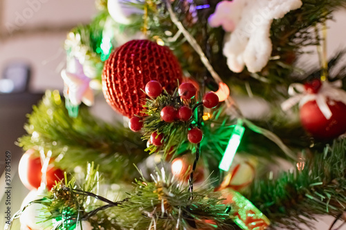 Bright red Christmas toys on the branches of an artificial Christmas tree. Snow balls and berries. A variety of festive accessories shimmer next to colored garlands and lanterns