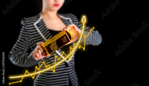 Growth of gold price graph chart to growth investors with businesswoman holding the gold bar on black background