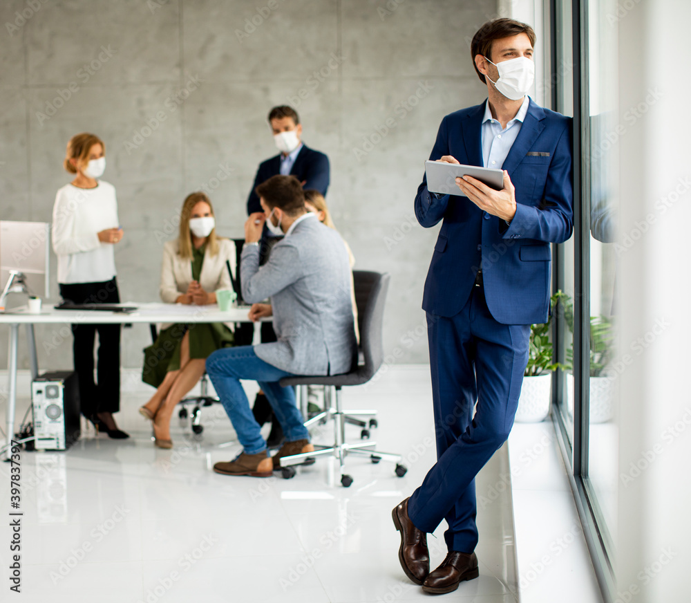 Handsome young business man wearing protective facial mask while holdind digital tablet