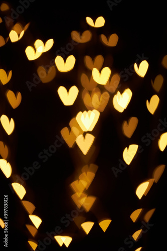 Gold bokeh in the shape of a heart. Festive background. Abstract holiday bokeh decorations Christmas glowing lights on black background. Golden abstract bokeh background. abstract grunge black backgro
