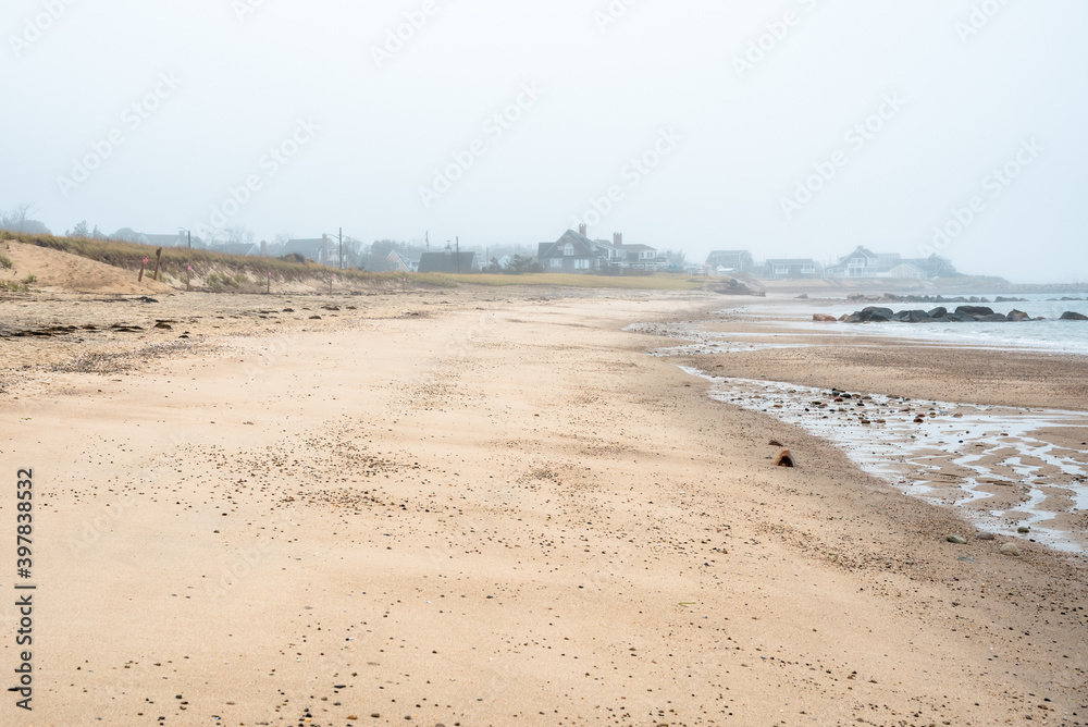 Empty sandy beach on a foggy autumn day. Oceanfront properties are visible in background. Sandwich, Cape Cod, MA, USA.