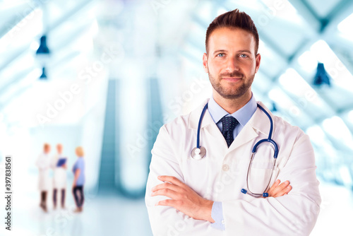 Confident male doctor standing with arms crossed in the hospital foyer