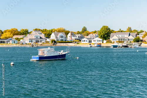 Empty boat moored off  a coast lined with residential buildings with private wooden jetties on a clear autumn day. Hyannis, Cape Cod, MA, USA.
