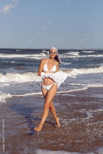 woman run in a white bathing suit and hat sunglasses on an empty sandy beach