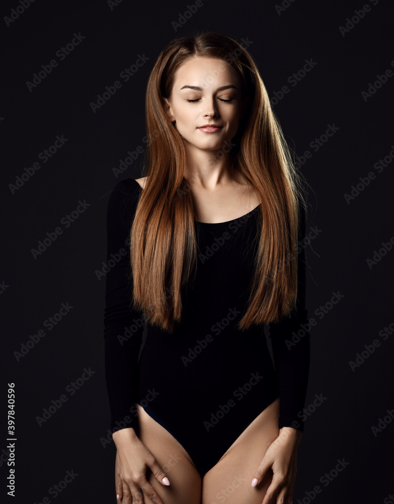 Young beautiful woman with long silky straight hair in black body with eyes closed standing and posing over dark background. Haircare, beauty, wellness concept Young beautiful woman with long silky straight hair in black body with eyes closed standing and posing over dark background. Haircare, beauty, wellness concept