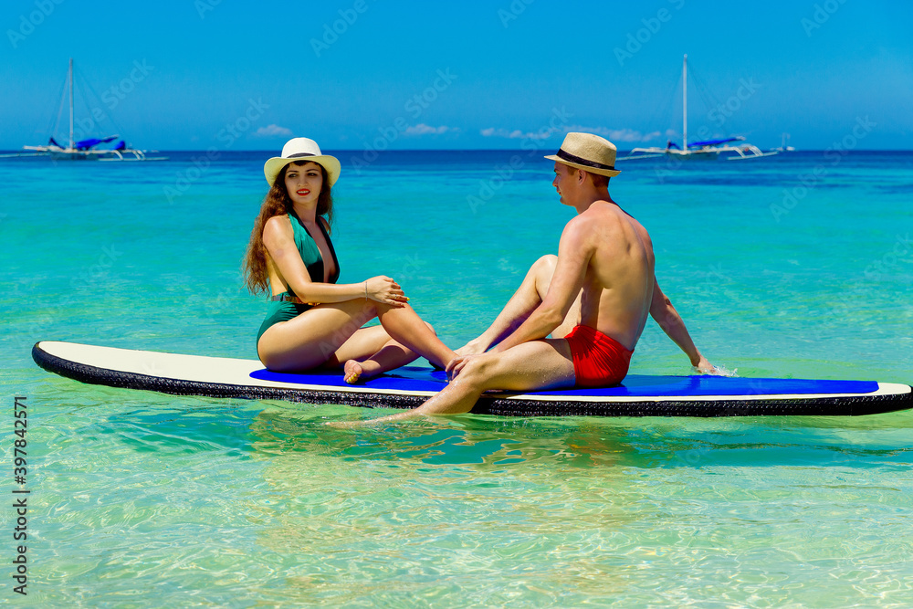 A happy couple in swimsuits have fun on a paddleboard in the tropical sea. The concept of travel and family holidays.