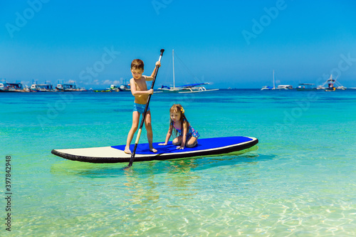 Smiling little girl and boy having fun on a paddleboard in the tropical sea. The concept of travel and family holidays.