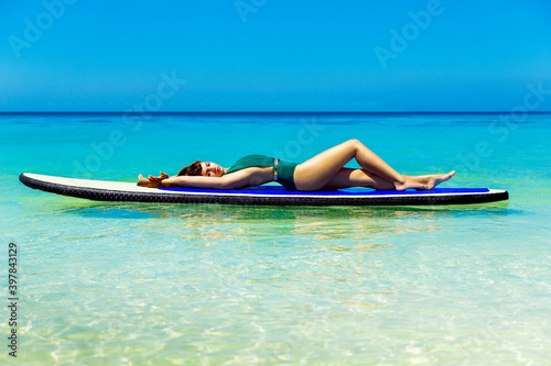 Beautiful brunette in swimsuits have fun on a paddleboard in the tropical sea. The concept of travel and beach holiday.
