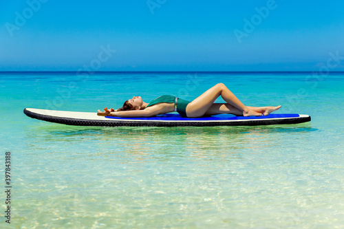 Beautiful brunette in swimsuits have fun on a paddleboard in the tropical sea. The concept of travel and beach holiday.