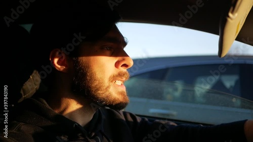 aggressive driver behind the wheel. Young bearded man swears at the wheel. Reckless Driving. The sunset rays of the sun penetrate the windshield