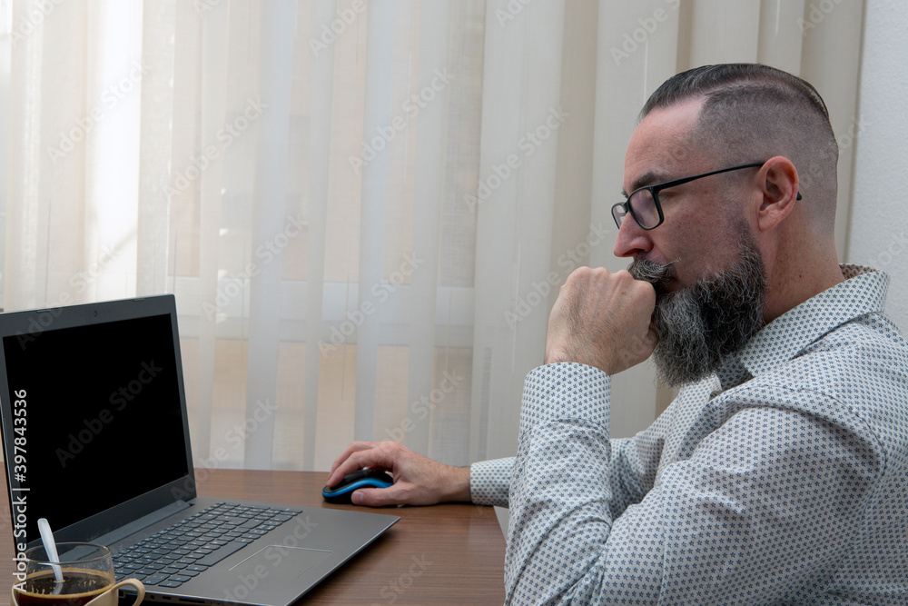 bearded man sitting in front of laptop working from home with notepad and a glass of coffee. bearded man sitting in front of laptop working from home with notepad and a glass of coffee.