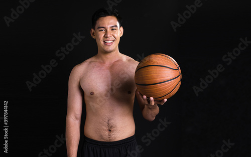 Portrait of asian muscular man standing and holding basketball on black background © Ann Rodchua
